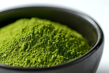 Vibrant green matcha tea powder in black ceramic bowl against white background, close-up view showing fine texture and natural organic appearance.