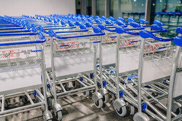 Rows of airport luggage trolleys with blue handles neatly arranged in a storage area. The metallic...