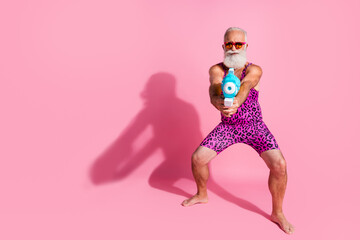 Full body photo of cool handsome old man have fun play serious watergun wear glamour leopard print overall isolated pink color background
