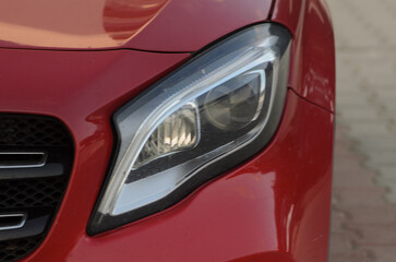 Detailed view showcasing the sleek headlight design of a red car parked in bright daylight
