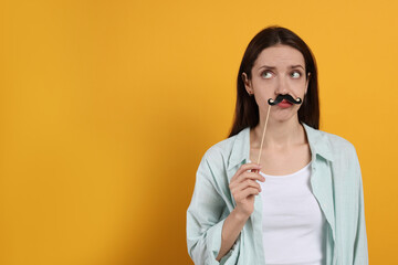 Thoughtful woman with fake paper mustache on orange background. Space for text