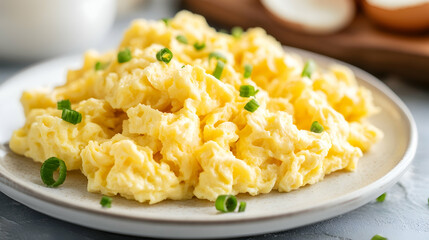 Fluffy scrambled eggs on a white plate symbolize simplicity and comfort in breakfast cuisine with a minimalistic bright tone and blurred empty caption space on the side