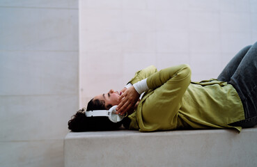 Happy woman lying on a bench, absorbed in high-quality audio through smart headphones. She enjoys...