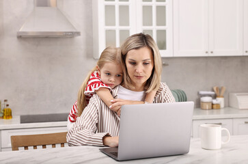 Work-family balance. Single mother working with laptop and her daughter at table in kitchen