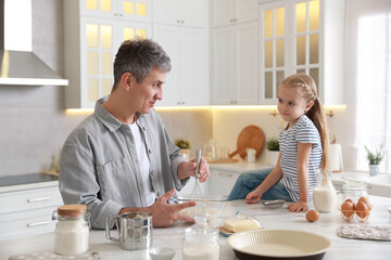 Father and his daughter making dough at white marble table in kitchen