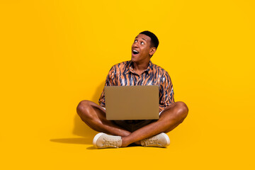 Young stylish man with a laptop looking amazed on a vibrant yellow background
