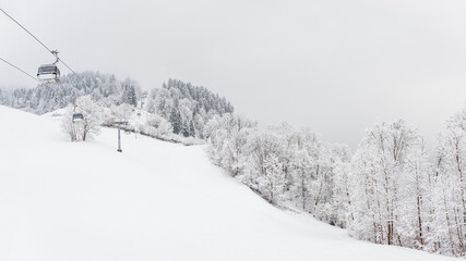 Winter landscape with snowy trees and a gondola railway to the top of the mountain, view during a mountain hike on a hiking trail. Winter day with cloudy and foggy weather.