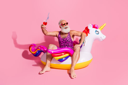 Elderly man in cheerful attire enjoying a fun summer day on a unicorn float with a drink in hand