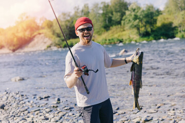Happy man fisherman holding freshly caught salmon fish from mountain river, Kamchatka Russia, concept fishing sport