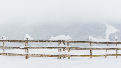 Snow-covered wooden fence on a mountain pasture. Winter landscape on a mountain hiking trail on a cloudy and foggy day.