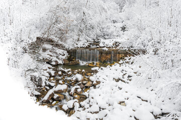 Mountain river in winter, water flows down the riverbed over snow-covered rocks. Winter landscape on a mountain hiking trail.