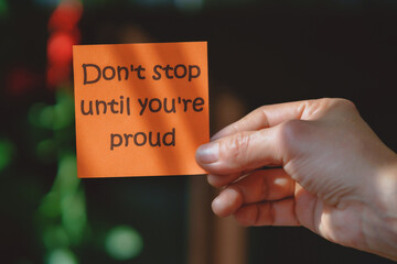 Colored paper note with masking tape with motivational phrases, hand holds a post it with blurred background, copy space.