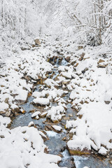 Mountain river in winter, water flows down the riverbed over snow-covered rocks. Winter landscape on a mountain hiking trail.