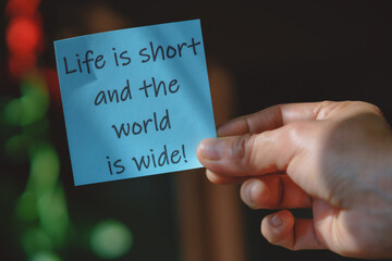 Colored paper note with masking tape with motivational phrases, hand holds a post it with blurred background, copy space.