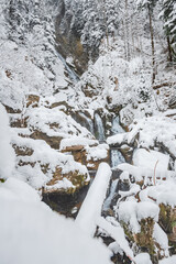 Mountain river in winter, water flows down the riverbed over snow-covered rocks. Winter landscape on a mountain hiking trail.