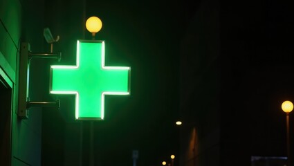 Obraz premium Neon medical bright glowing illuminated pharmacy cross sign with green and red light bulbs on building at night during pandemic quarantine.