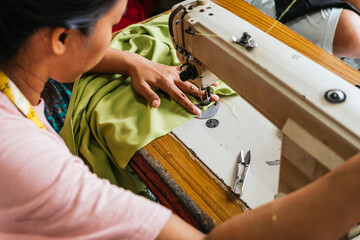 Asian seamstress works with sewing machine and green fabric