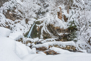 Mountain river in winter, water flows down the riverbed over snow-covered rocks. Winter landscape on a mountain hiking trail.