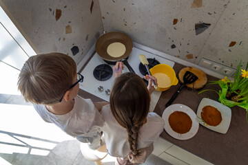 Children Cooking Pancakes Together in Kitchen. Two children stand by a stove, making pancakes...