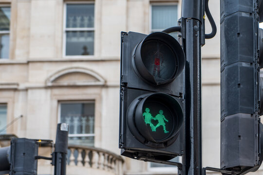 A pedestrian traffic light in London displays a green signal with two walking figures. A historic building is visible in the background.