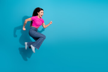 Cheerful young woman in a vibrant outfit joyfully jumping with enthusiasm on a blue background,...