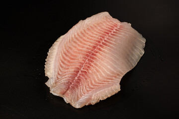 Fresh tilapia fillet on black background, top view.