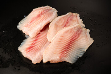 Fresh tilapia fillet on black background, top view.