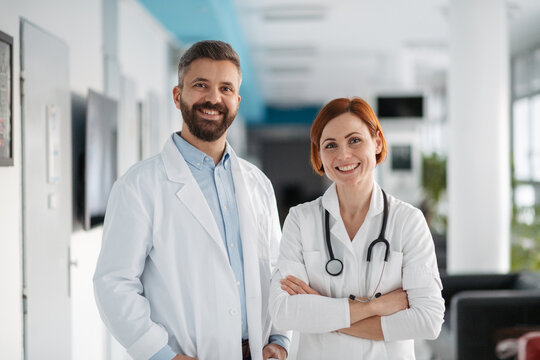 Portrait of two doctors in hospital hallway, holding medical records in hand.