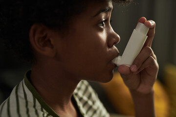 Close-up of face of youthful boy with asthma attack pumping inhaler in mouth while watching...