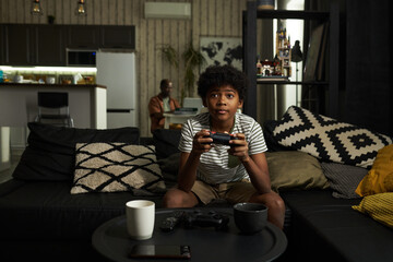 Cute youthful African American boy pressing buttons on gamepad and looking at screen of tv set while playing video game © pressmaster