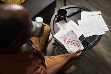 Above view of mature African American man with inhaler and overdue bill in hands sitting by table...