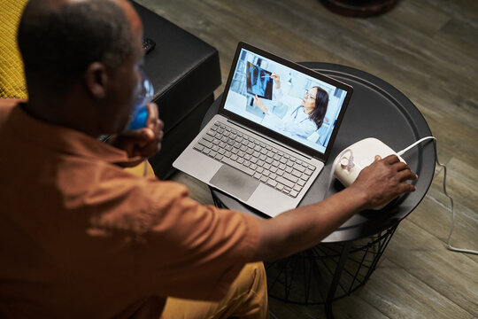 High angle of African American man with nebulizer holding mask by his face during medical treatment and online consultation