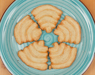 Five palmier cookies arranged in a circular pattern on a light blue plate, set against a wooden surface