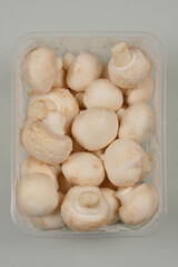 A top-down shot of a clear plastic container filled with fresh white button mushrooms