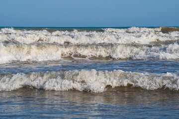 A light storm on the Spanish coast. Sea waves with crests of white foam roll onto a sandy beach on...