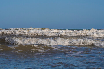 A light storm on the Spanish coast. Sea waves with crests of white foam roll onto a sandy beach on...