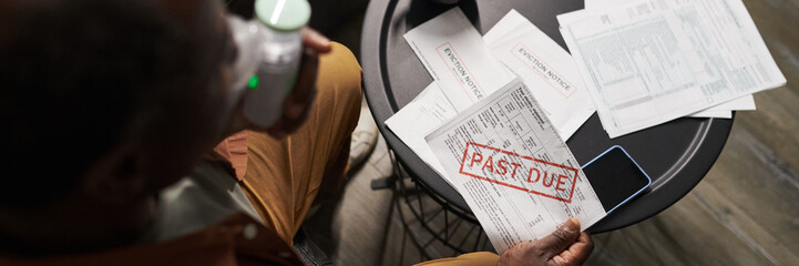 Header of mature African American man with inhaler and overdue bill in hands sitting by table with...