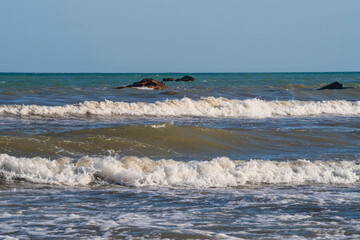 A light storm on the Spanish coast. Sea waves with crests of white foam roll onto a sandy beach on a clear day.
