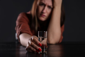 Alcohol addiction. Miserable woman with vodka at table in dark, selective focus