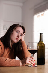 Alcohol addiction. Miserable woman with wine at table indoors, selective focus