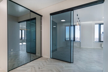 A spacious, bright hall with a mirrored wardrobe and a sliding glass door in a luxurious mansion. Light parquet, unfurnished.