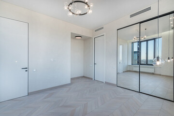 A hall with a mirrored wardrobe in a luxury apartment. Light parquet. Unfurnished.