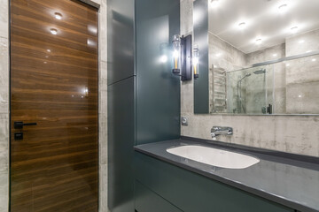 Brown entrance door in the bathroom with gray furniture. A large mirror, a wall lamp stylized as a...