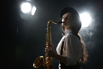 Fototapeta premium Professional musician playing saxophone on dark background with lights and smoke. Space for text
