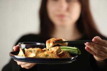 Woman holding tasty fried gyoza (dumplings) on white background, selective focus