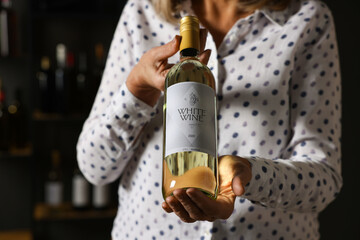 Professional sommelier holding bottle of white wine indoors, closeup