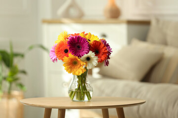 Bouquet of beautiful gerbera flowers in glass vase on wooden table indoors