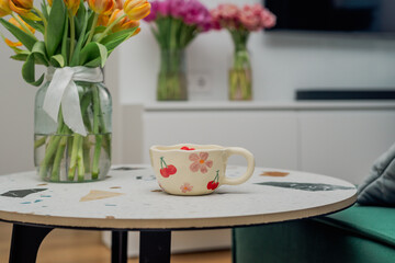 A patterned cup on a living room table with flowers