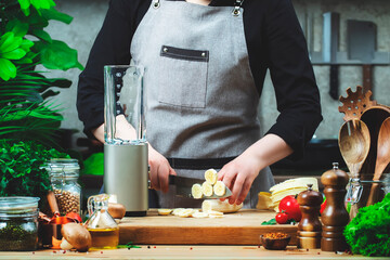 Chef  cuts bananas for prepare smoothie in blender. Cozy kitchen with wooden table, kitchenware,...