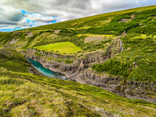 A scenic view of Studlagil Canyon in Iceland with basalt columns and a turquoise river.
